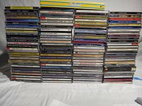 Photo showing multiple stacks of music CDs in jewel cases arranged in several columns on a plain background