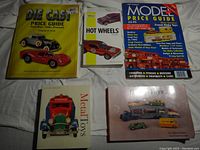 Top view of all 5 diecast car collector books laid on a bed, showing front covers of titles including Die Cast Price Guide, Hot Wheels, Model Price Guide, Metal Toys, and Dinky Toys.