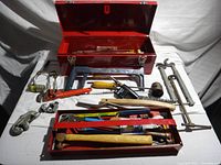 Photo of the open red metal toolbox with various plumbing tools arranged inside and around it