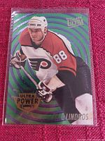 Front view of 1994-1995 Fleer Ultra Ultra Power Eric Lindros hockey card in protective sleeve showing player in Philadelphia Flyers uniform on a green swirl background.