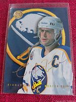 Close-up photo of the 1993/1994 Leaf Studio Signature Series hockey card featuring a Buffalo Sabres player with captain's C on jersey, in protective plastic sleeve on red fabric background.
