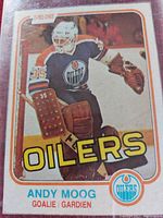 Photo of O-Pee-Chee hockey card showing Andy Moog in goalie gear for Edmonton Oilers, card front face visible with branding and player information.