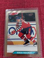 Close-up photo of Sergei Fedorov hockey card in a plastic sleeve on red fabric background.