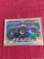 Holographic Upper Deck Defense Mechanism hockey card showing seven Vancouver Canucks players, including Quinn Hughes, in blue uniforms with a reflective background.