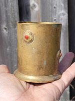 Side view of antique brass pen holder showing red gemstone inlay on circular brass ornamentation.