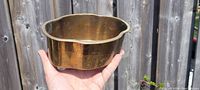 Brass flower pot held in hand showing size and finish under natural light.