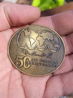 Front side of bronze medallion showing stylized world map and '50th Golden Anniversary' inscription.