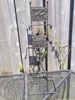 Black metal display stand featuring two embossed panels with elephants and trees, several hooks for hanging items, and a triangular base for stability. Approximate height 24 inches.
