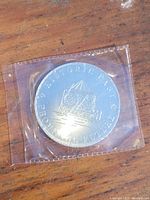 Photo of coin reverse side showing building and globe design with text "Restorist Pint Frontenac Dollar"