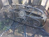 Metal pot rack laid flat showing decorative scrollwork and central floral medallion on metal mesh base.