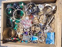 Wooden box filled with assorted vintage costume jewelry including bracelets, necklaces, earrings, and pendants in varied colors and styles