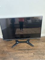 Front view of Sharp TV on stand with remote control in front
