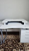 Full view of the white adjustable desk top mounted on a desk with drawers and metal legs, showing size and placement.