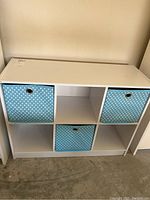 Front view of white shelf unit with three blue polka dot fabric bins in three compartments