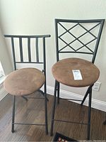 Two brown padded folding stools side by side, one taller with lattice back and another smaller with simple bar backrest.