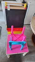 Photo of children's easel showing blackboard surface, red and yellow plastic frame, and attached trays
