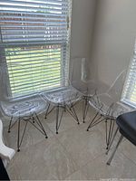 Four clear chairs with metal wire bases arranged near windows providing natural light.