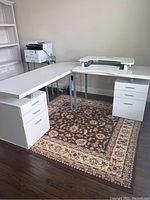 Full view of the L-shaped white office desk setup with two storage pedestal drawers and an additional desk riser (not included)