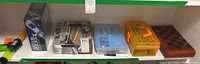 Shelf with various kits and games including the Mega 2560 starter kit, the electricity and magnifying kits in plastic boxes, water rocket boxed kit, and chess/checker wooden board