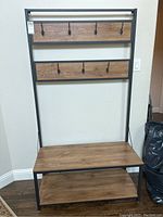 Front view of the hall bench showing wood seat and two rows of hooks on wood panels within black metal frame.