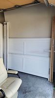 King-size white wooden headboard and footboard leaning against wall with bed rails adjacent, in garage storage area.