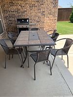 Full view of rectangular patio table with stone tile top and umbrella hole surrounded by eight brown resin woven patio chairs.