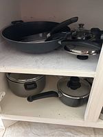 Shelves with assortment of pots, pans and skillets with lids, black handles visible