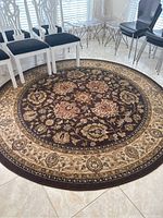 Overview of the round brown rug placed on a tiled floor surrounded by chairs, showing the full design and size.