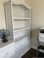 Front angle view of white wooden storage cabinet with three shelves, two drawers, and lower storage cabinet.
