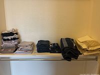 View of multiple neatly folded towels and wash cloths in beige, gray, dark blue, and black, arranged on a closet shelf.