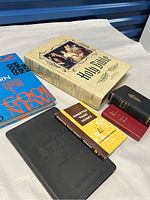 Photo showing seven religious books including the large Catholic Holy Bible, Good News Bible, and other devotional books on white cloth background.