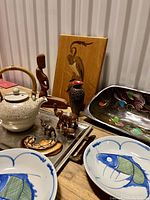 Wide view of eclectic boho lot showing pottery teapot, carved wooden bird plaque, carved wooden figures, Restoration Hardware tray, and fish painted ceramic bowls