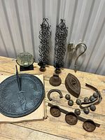 Photo showing entire lot including cast iron sundial on cardboard, wrought iron candle sconces, antique sad iron, horseshoes, cowbells and triple measuring scoop.
