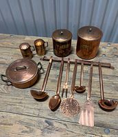 Full view of all items laid out: two canisters with lids, salt and pepper shakers, artisan copper pot with lid and handles, six copper hanging kitchen utensils, copper rack.