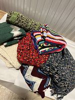 Seven handmade crochet blankets folded and laid out on a white surface showing variety in color and texture.