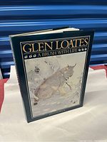 Front angled view of Glen Loates hardcover art book with dust jacket showing title and a lynx in snow illustration.
