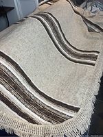 Photo showing beige woven table linen with dark and white horizontal stripes and fringe along one edge, highlighting texture and pattern