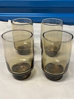 Four Libbey mid-century modern smoky brown glass tumblers on a white cloth, viewed from an angle showing their cylindrical shape and thicker base.