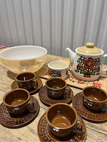 Overall view of the lot showing Fireking peach lustre mixing bowl, retro teapot, sugar container, and five espresso cups with saucers arranged on wooden tabletop.