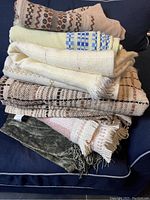 Photo of stacked woven vintage linens showing various patterns in neutral and pastel colors, including a predominantly green textile at bottom.