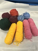 Photo showing 10 assorted yarn skeins and balls in yellow, pink, blue, green, orange, and reddish-brown shades.