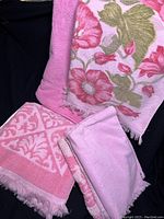 Photo showing several vintage pink towels folded, including a floral design towel and solid pink towels with decorative fringes.