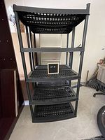 Front view of one black plastic shelving unit showing five slotted shelves, matte black finish, and sturdy construction.