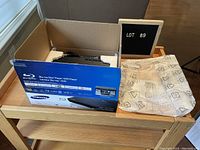 Samsung Blu-ray player in original blue retail box with foam inserts and protective wrapping paper on a wooden table.