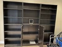 Front view of three dark brown IKEA Billy bookcases, the center one has cabinet doors open showing interior shelves and visible shelf damage on one shelf.