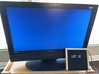 Front view of Digistar LCD TV model LC-2710D powered on showing blue screen with the model and HDMI branding visible on the bezel, placed on wooden surface.