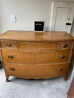 Front view of mid century modern dresser showing top two drawers separated and original oval metal pulls. The wood surface shows wear and scratches.