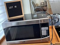 Oster microwave oven front left angled view showing keypad, door, and cord.