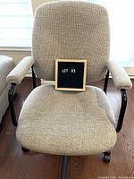 Front view of light beige upholstered office chair showing the fabric, padded armrests, and wheels.