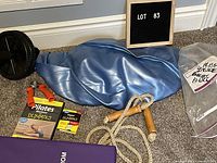Photo showing blue deflated fitness ball, black ab roller wheel, wooden handled jump rope, Pilates Workout for Dummies DVD case, and part of purple foldable mat.